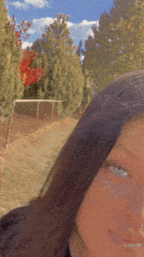 a close up of a girl 's face with a blurred background of trees