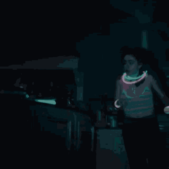 a woman is dancing in the dark with glow in the dark bracelets around her neck