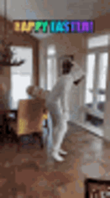 a person in a white suit is dancing in a living room with a happy easter sign above them .