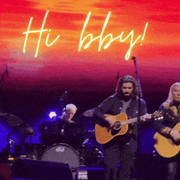 a man playing a guitar on a stage with the words hi baby behind him