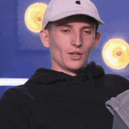 a man wearing a white hat and a black hoodie looks at the camera