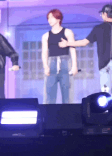 a man in a black tank top is standing on a stage with two other men