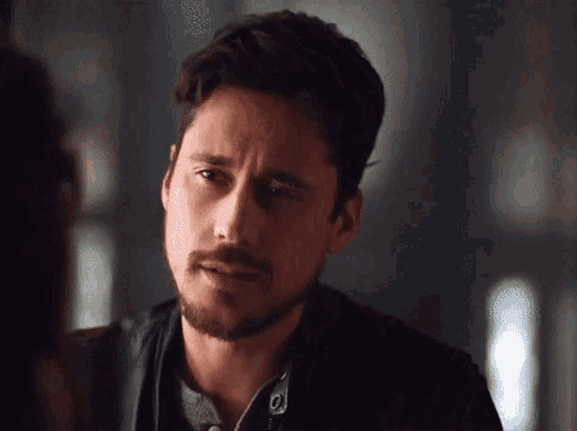 a man with a beard and a leather jacket looks at another man