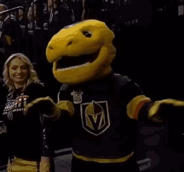 a woman is standing next to a yellow mascot in a hockey arena .
