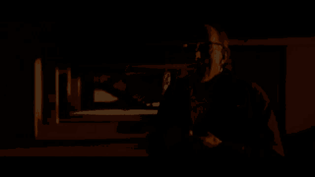 a man with glasses is standing in a dark room with his hand in his mouth .