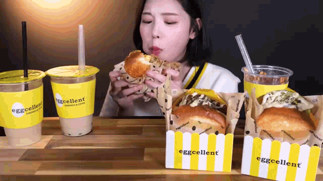 a woman is eating a sandwich and drinking eggcellent coffee