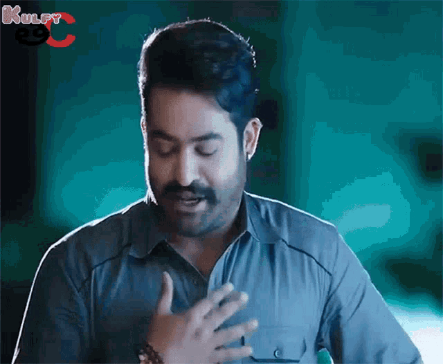 a man with a mustache is making a funny face with his hands on his chest .