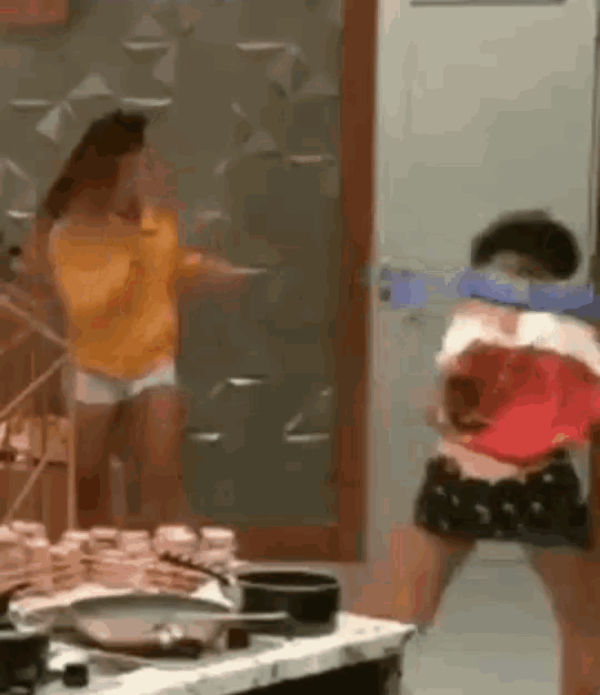 a woman in a yellow sweater is standing next to a woman in a red shirt in a kitchen .