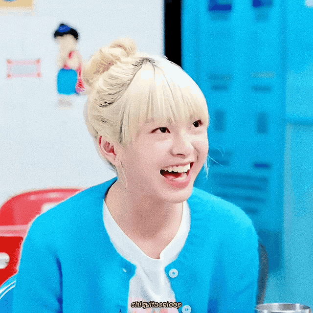a girl with blonde hair wearing a blue cardigan and a white shirt is smiling