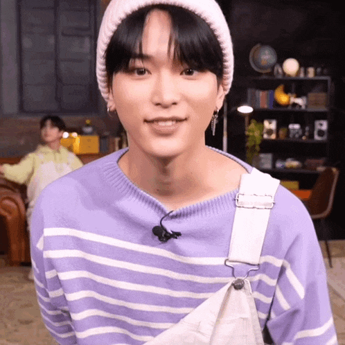 a young man wearing a purple striped sweater and overalls is smiling