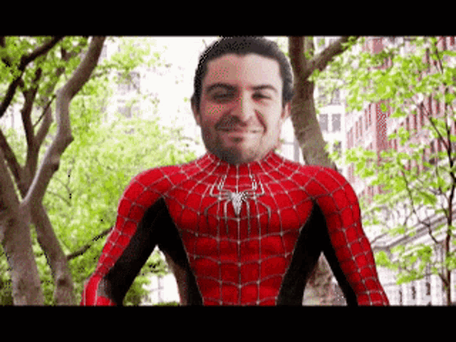 a man in a spiderman costume stands in front of trees and a building