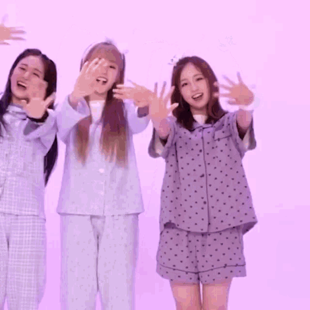 three girls in pajamas are making a heart with their hands .