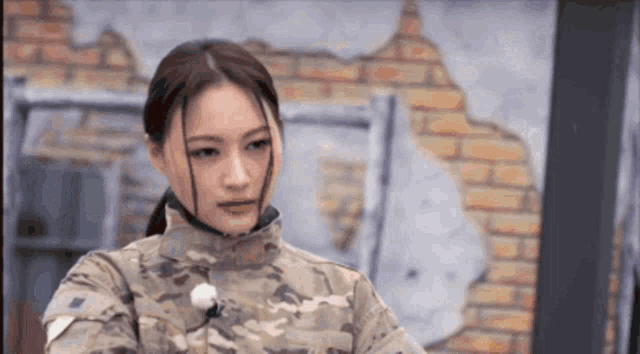 a woman in a military uniform is standing in front of a brick wall looking at the camera .