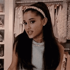 ariana grande is wearing a headband and earrings while standing in front of a closet .