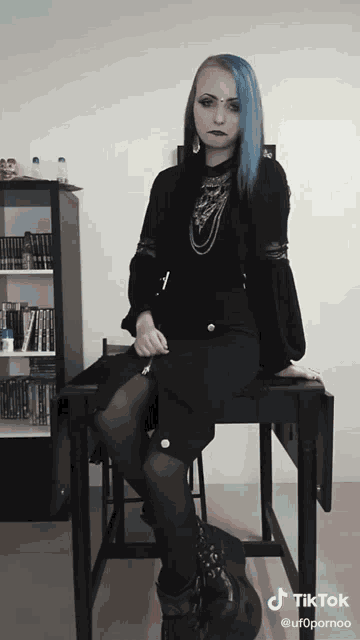 a woman with blue hair is sitting on a table with tiktok written on the bottom right