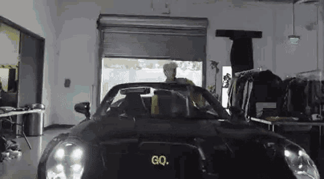 a man is driving a black sports car in a garage with the words go on the hood .