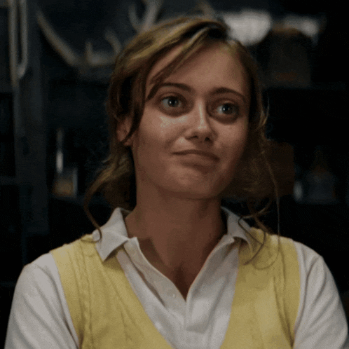a woman wearing a yellow vest and a white shirt is smiling