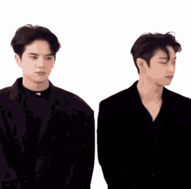 two young men in black suits are standing next to each other .