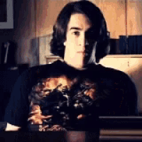 a man wearing headphones and a black shirt is sitting at a table in a dark room .