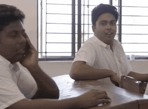 a man talking on a cell phone next to another man sitting at a desk