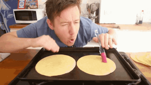 a man in a blue shirt is making tortillas on a tray