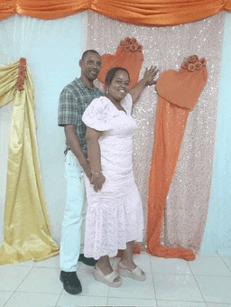 a man and woman posing for a picture in front of a heart shaped backdrop