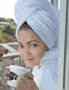 a woman with a towel wrapped around her head is holding a cup