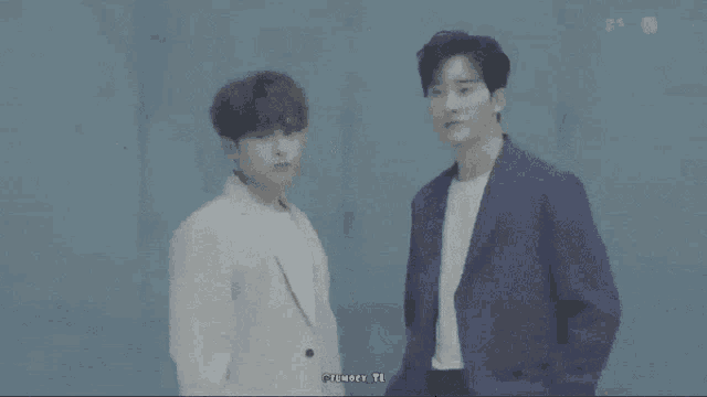 two men are standing next to each other with their fingers in the shape of hearts