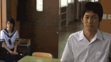 a boy in a white shirt sits at a desk in front of a girl sitting on a chair