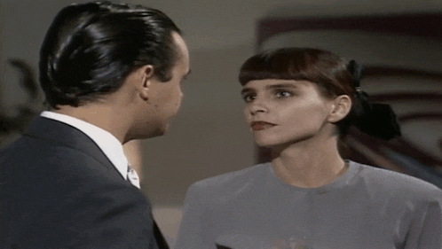 a man in a suit and tie stands next to a woman in a gray shirt