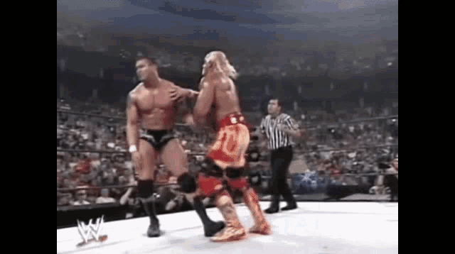 two wrestlers are fighting in a wrestling ring with a referee watching .