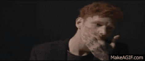 a man with red hair is covering his mouth with his hand while smoking a cigarette .