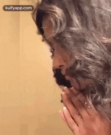 a woman with long hair and a beard is praying with her hands folded in front of her face .