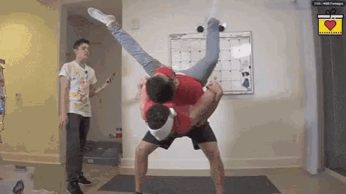 a man is holding another man upside down in his arms while another man looks on .