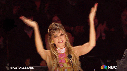 a woman stands in front of a microphone with her arms in the air and the nbc logo in the corner