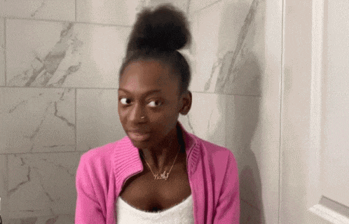 a woman in a pink sweater is making a funny face while standing in front of a marble wall .