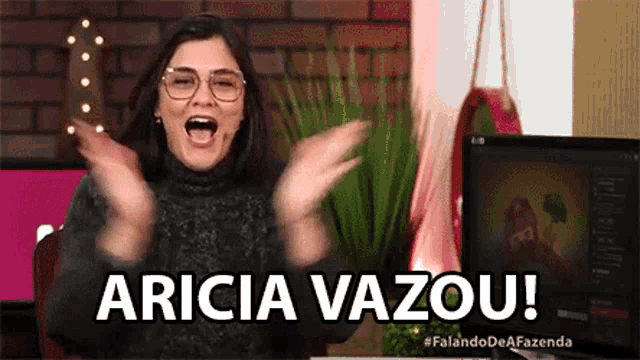 a woman wearing glasses and a black sweater is sitting in front of a computer and making a funny face .