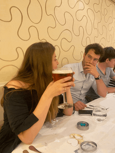 a woman drinking a glass of beer while sitting at a table with other people