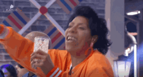 a woman in an orange jacket is smiling and holding a glass of water .
