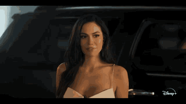 a woman in a white dress is standing in front of a car with disney + written on the bottom