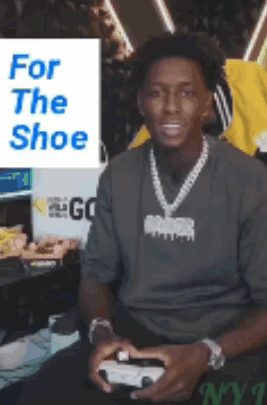 a man is holding a video game controller while wearing a necklace and a gray shirt .