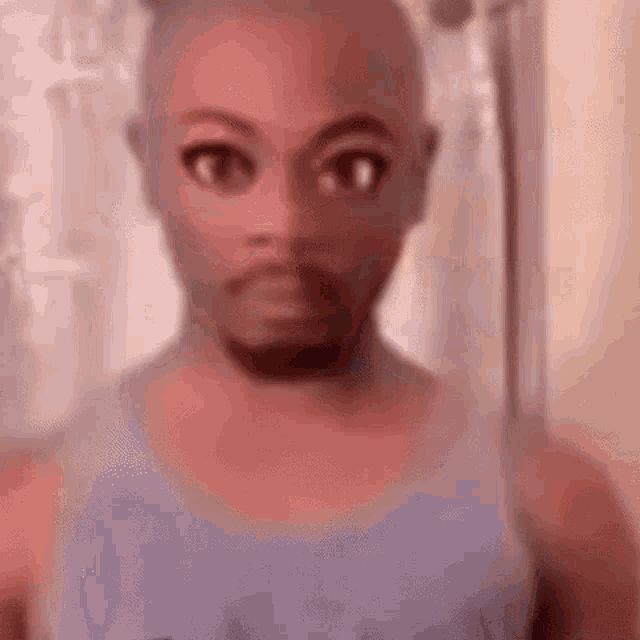 a man with a beard is wearing a purple tank top and looking at the camera .