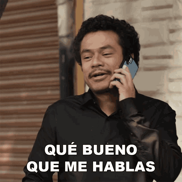 a man in a black shirt talking on a cell phone with que bueno que me hablas below him