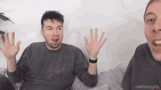 two men are sitting next to each other on a bed and one of them is making a surprised face .