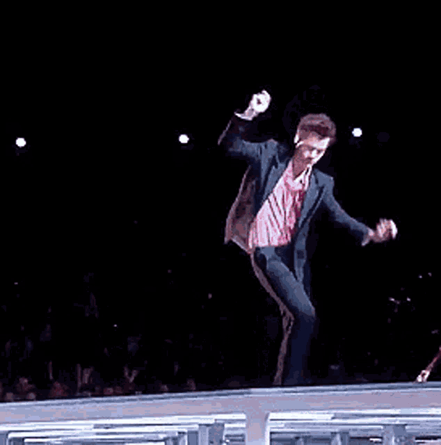 a man in a pink shirt is dancing on a stage while a man in a red suit is playing a guitar .