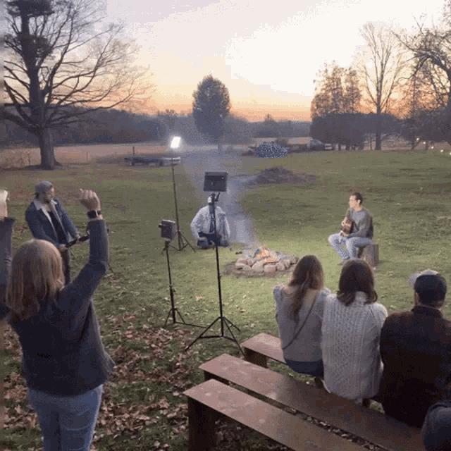 a group of people watching a man play a guitar by a fire pit