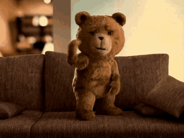 a teddy bear is standing on a couch and making a funny face