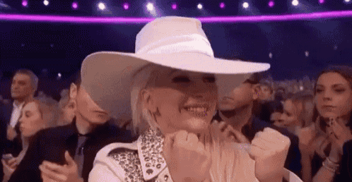 a woman wearing a white hat and a white jacket is sitting in a crowd of people .