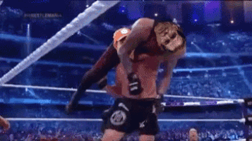 a man is wrestling another man in a boxing ring while wearing a championship belt .