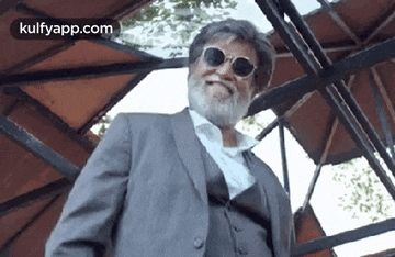 a man with a beard wearing sunglasses and a suit is standing under a gazebo .